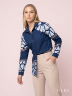 Woman wearing a blue patterned shirt and beige pants on a pink background with 'VYBE' branding.
